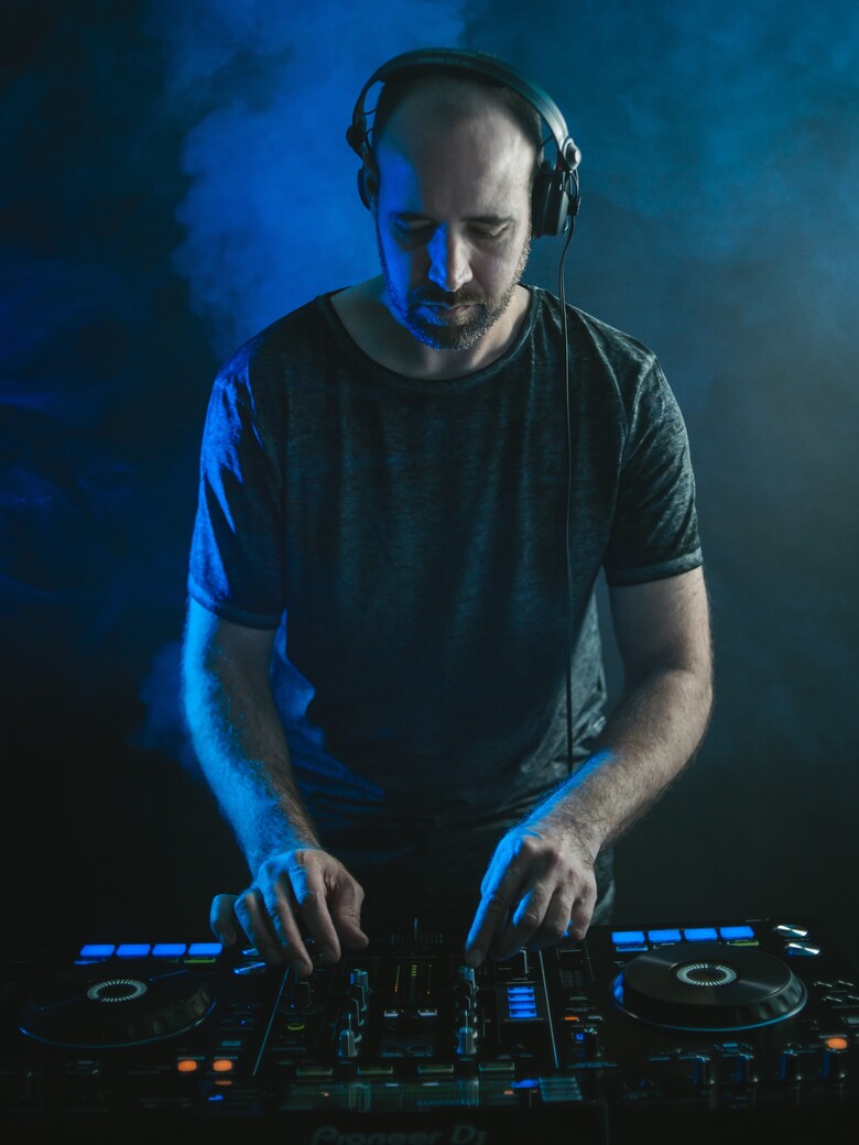 A vertical picture of a male DJ playing music under the lights against a dark background in a studio